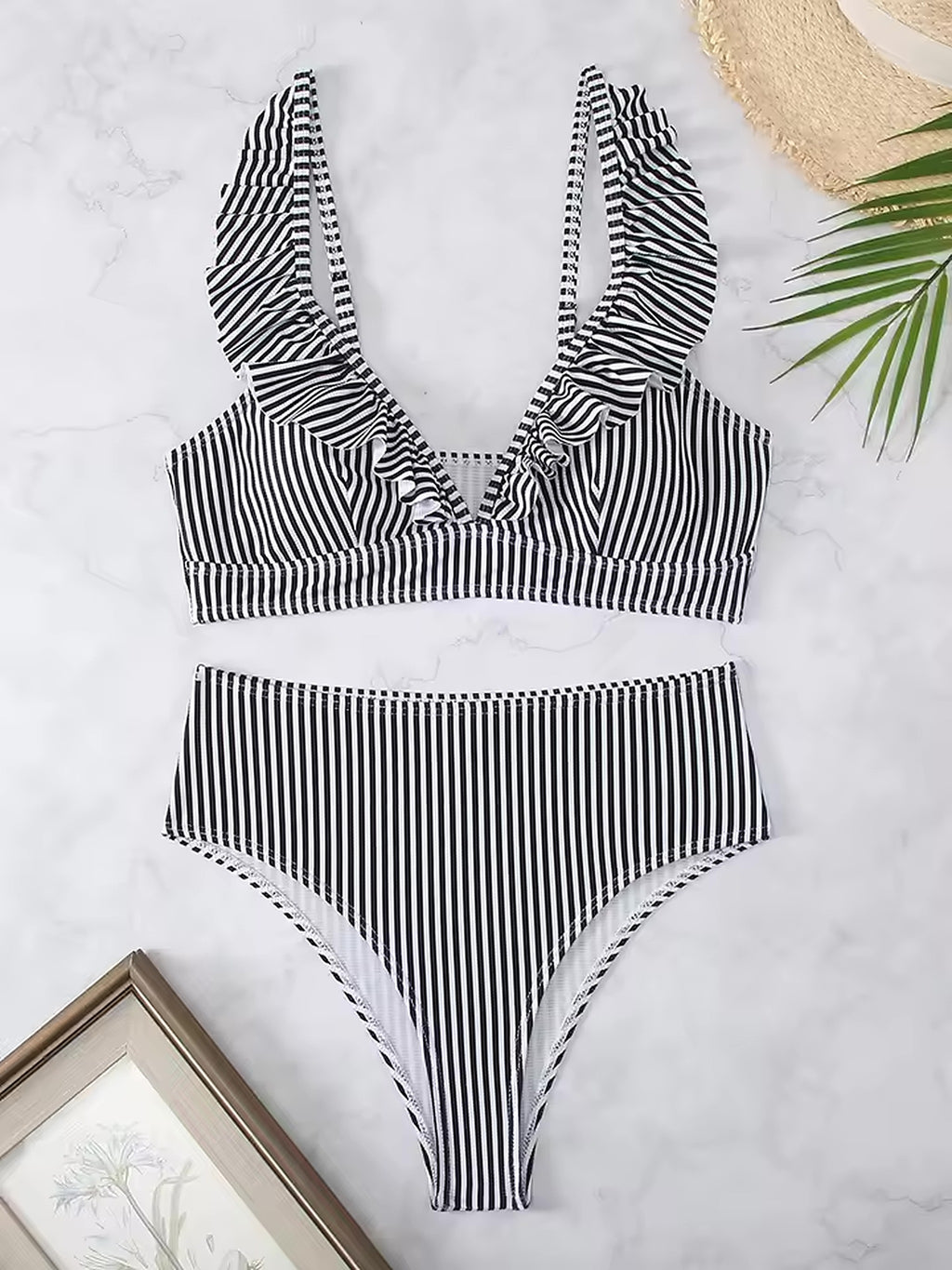 Black and white striped bikini with ruffled neckline and high-waisted bottoms on marble background with beach accessories