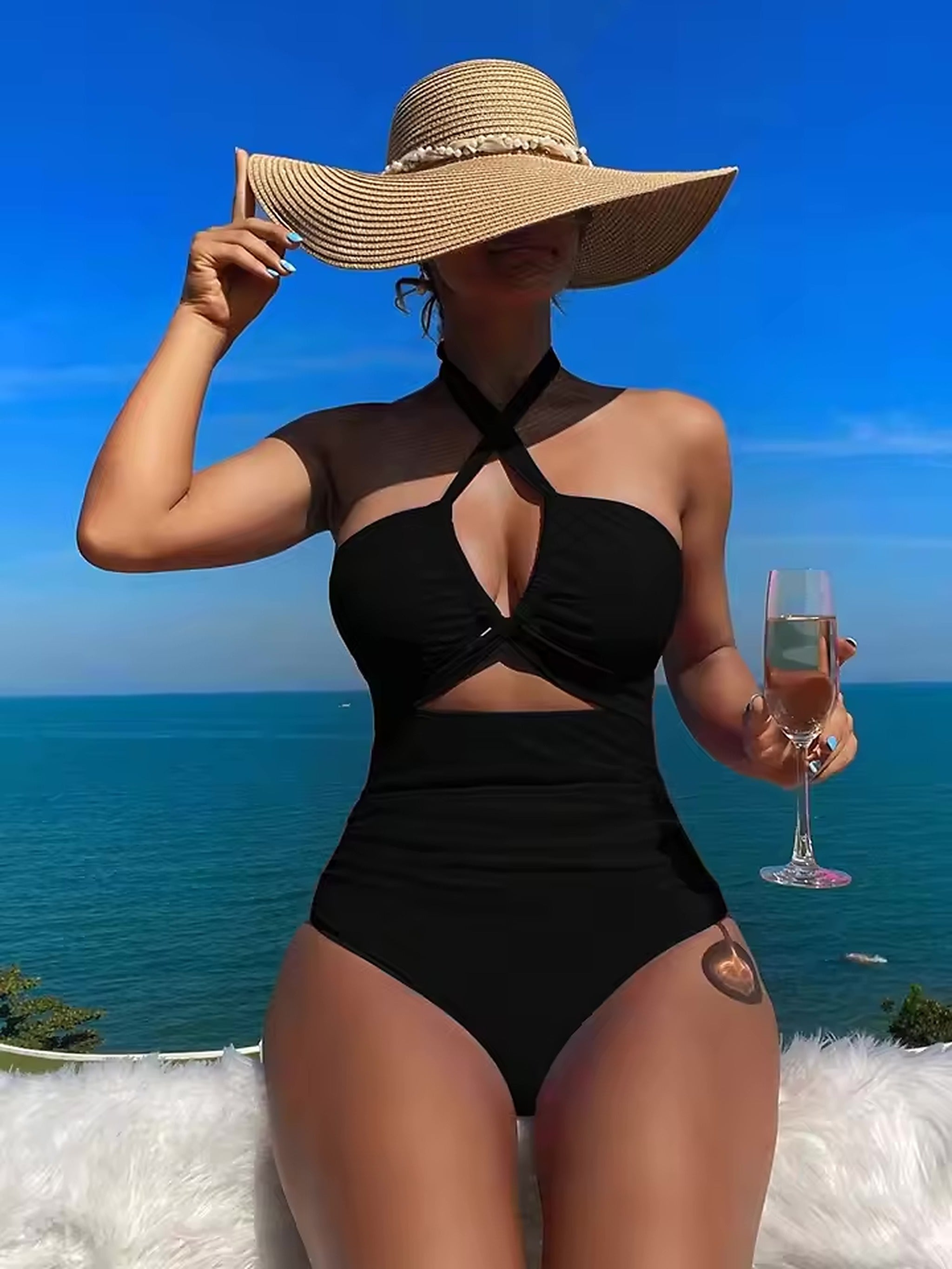 Woman wearing black halter cutout bikini top and high-waisted bikini bottoms by ocean, holding wide-brimmed straw hat and