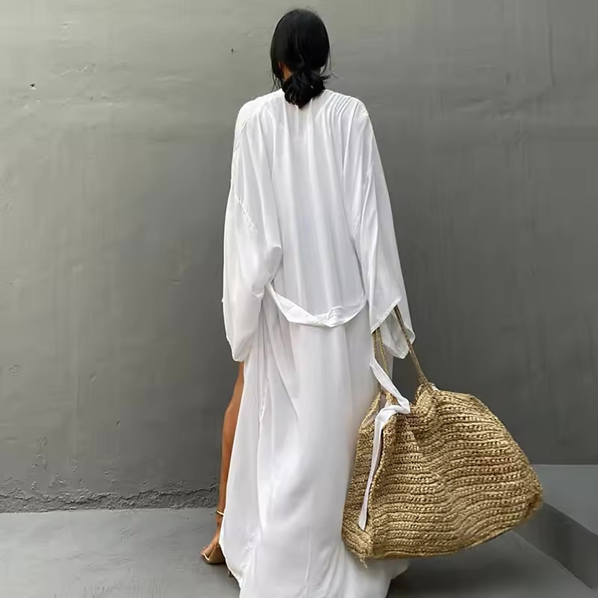 Woman wearing white Luna Mare cover-up over swimwear, holding woven beach bag, rear view