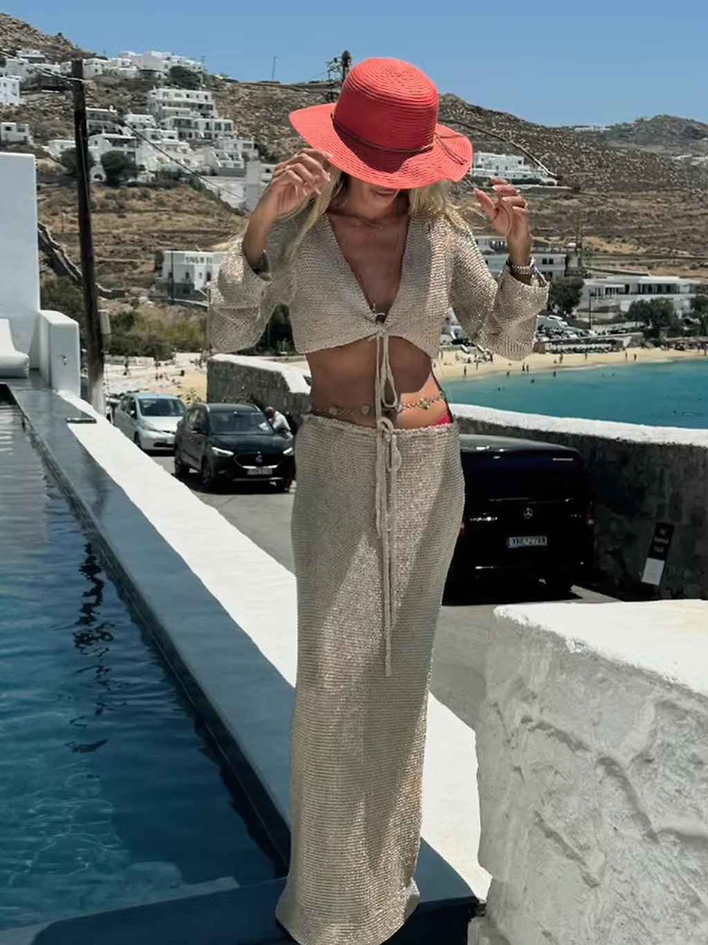 Woman wearing beige knit bikini top and matching sarong with coral sun hat by Mediterranean coastline
