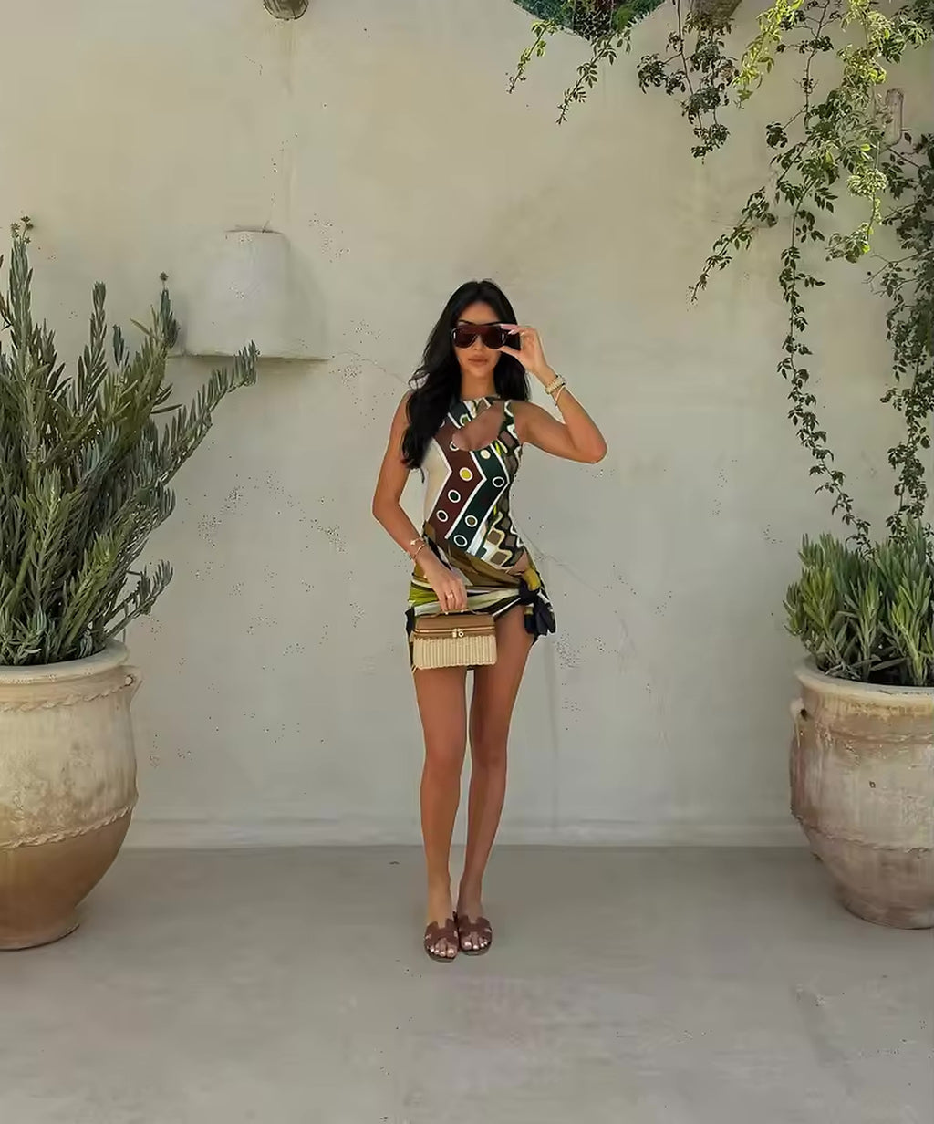 Woman wearing geometric patterned bikini top with fringe skirt, styled with sunglasses and accessories in minimalist garden