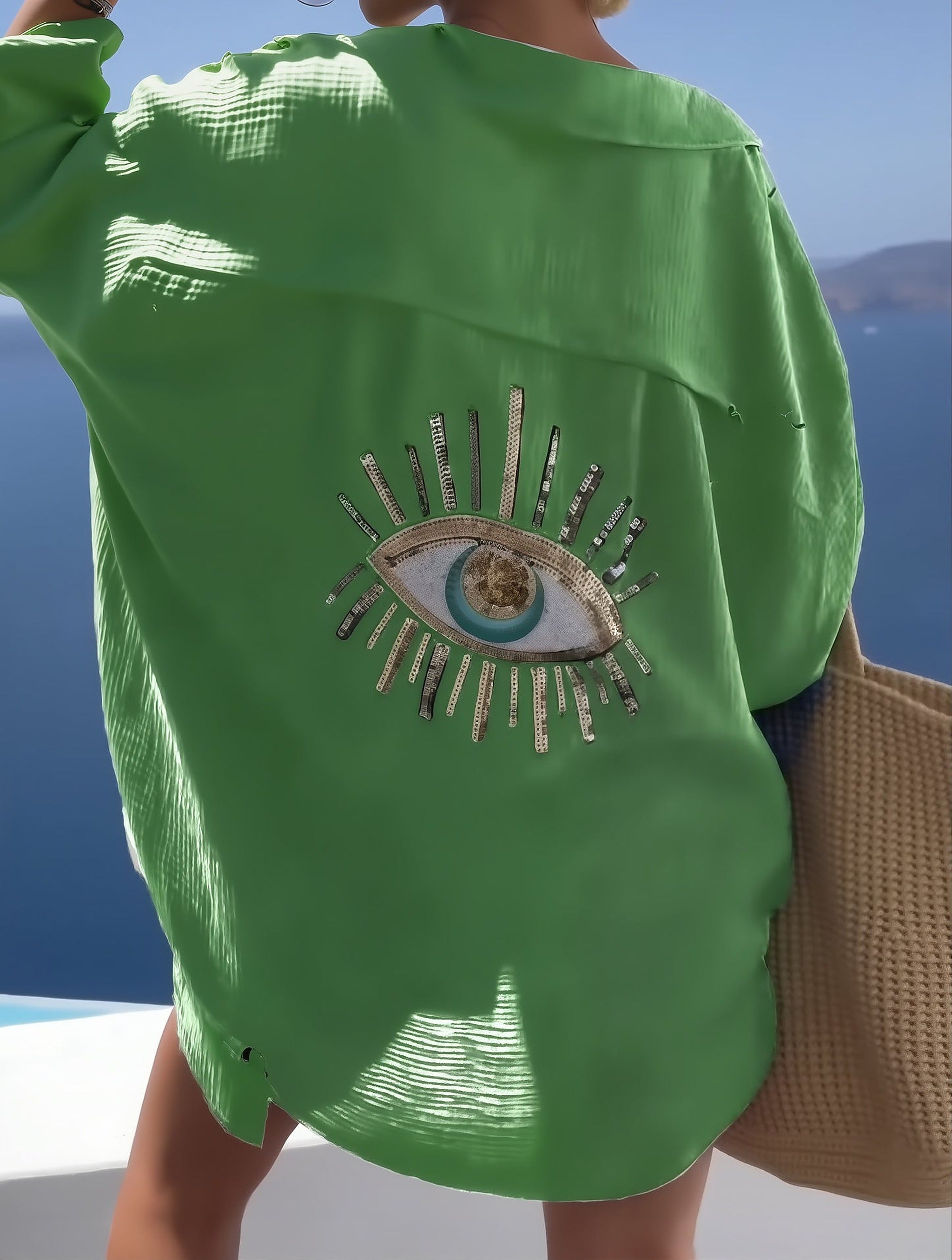 Green Costa Coral bikini with embellished eye motif on back, worn by model overlooking blue sea.