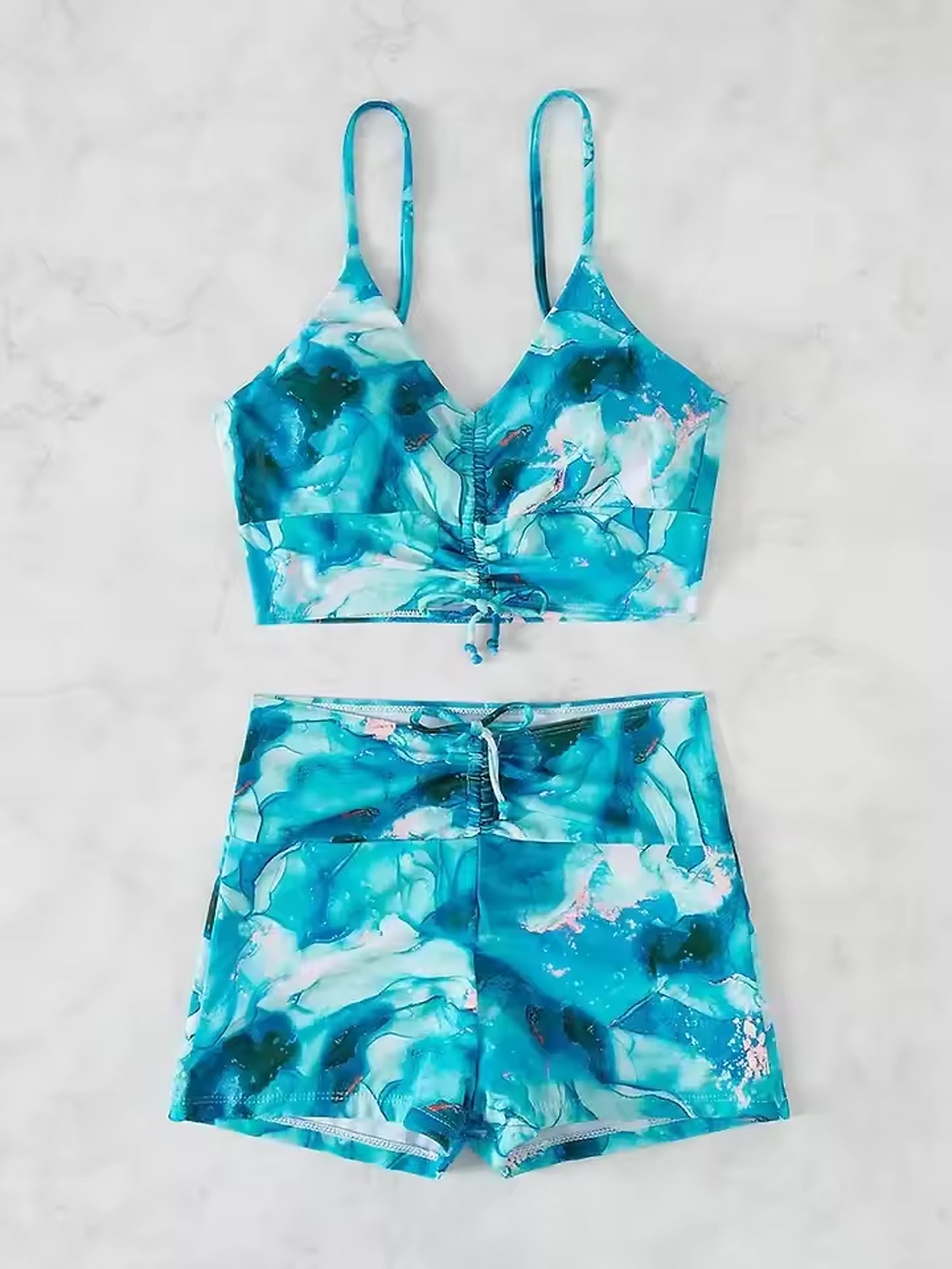 Turquoise abstract print bikini with adjustable straps and matching shorts on marble background