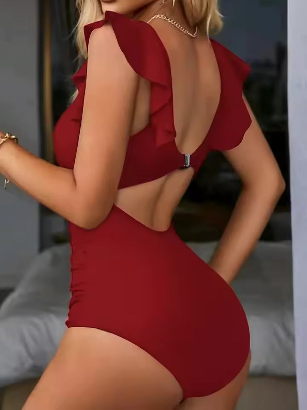 Burgundy one-piece swimsuit with ruffled back detail and open cutout, worn by model against neutral background.