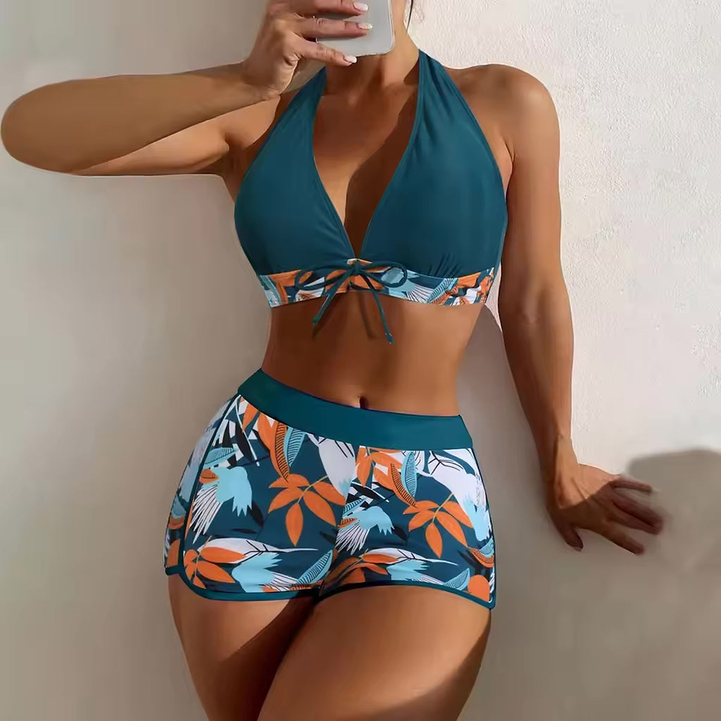 Teal halter bikini top with tropical print band and matching patterned shorts featuring orange and blue botanical design.