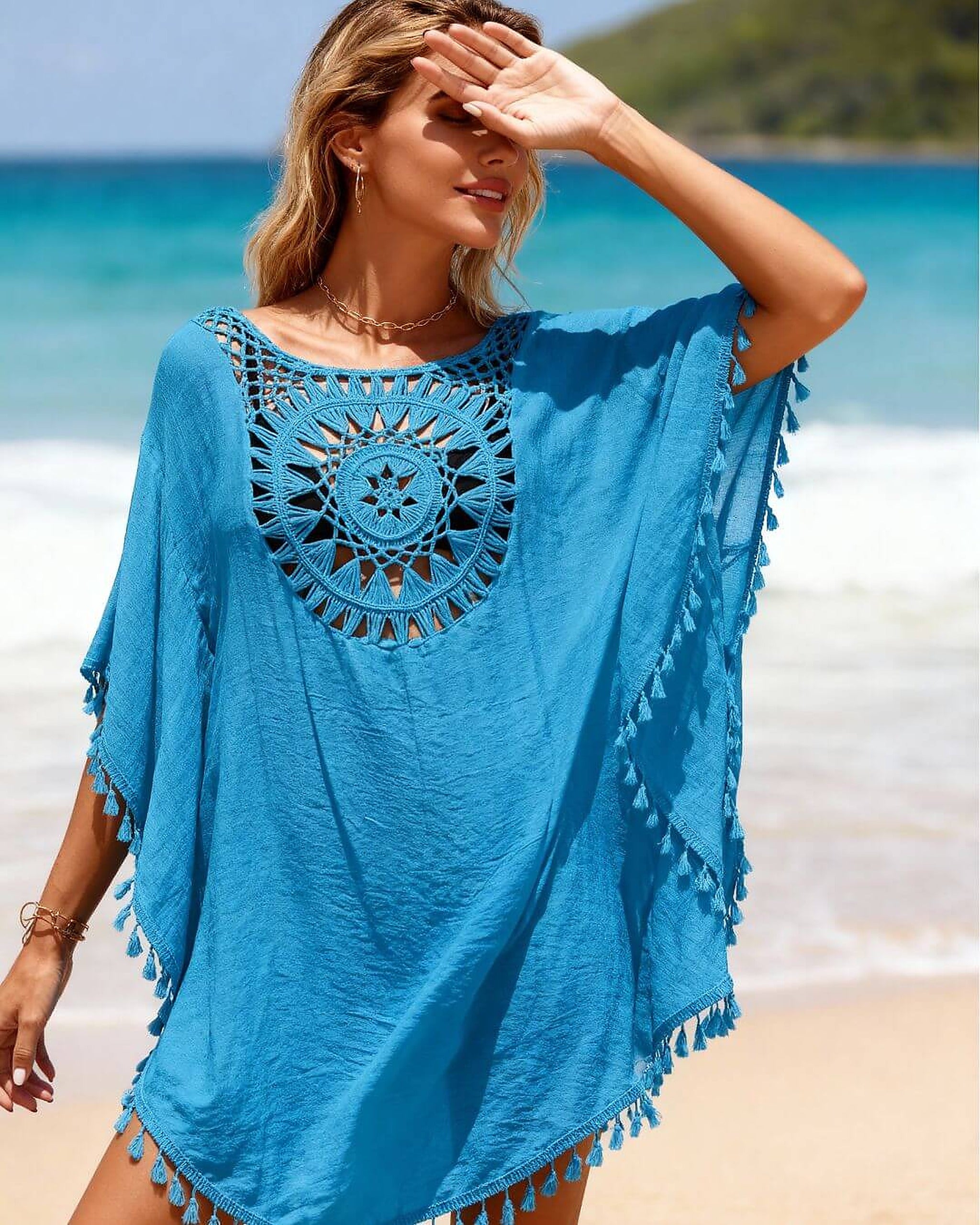 Woman wearing blue crochet beach dress with tassels on sandy beach