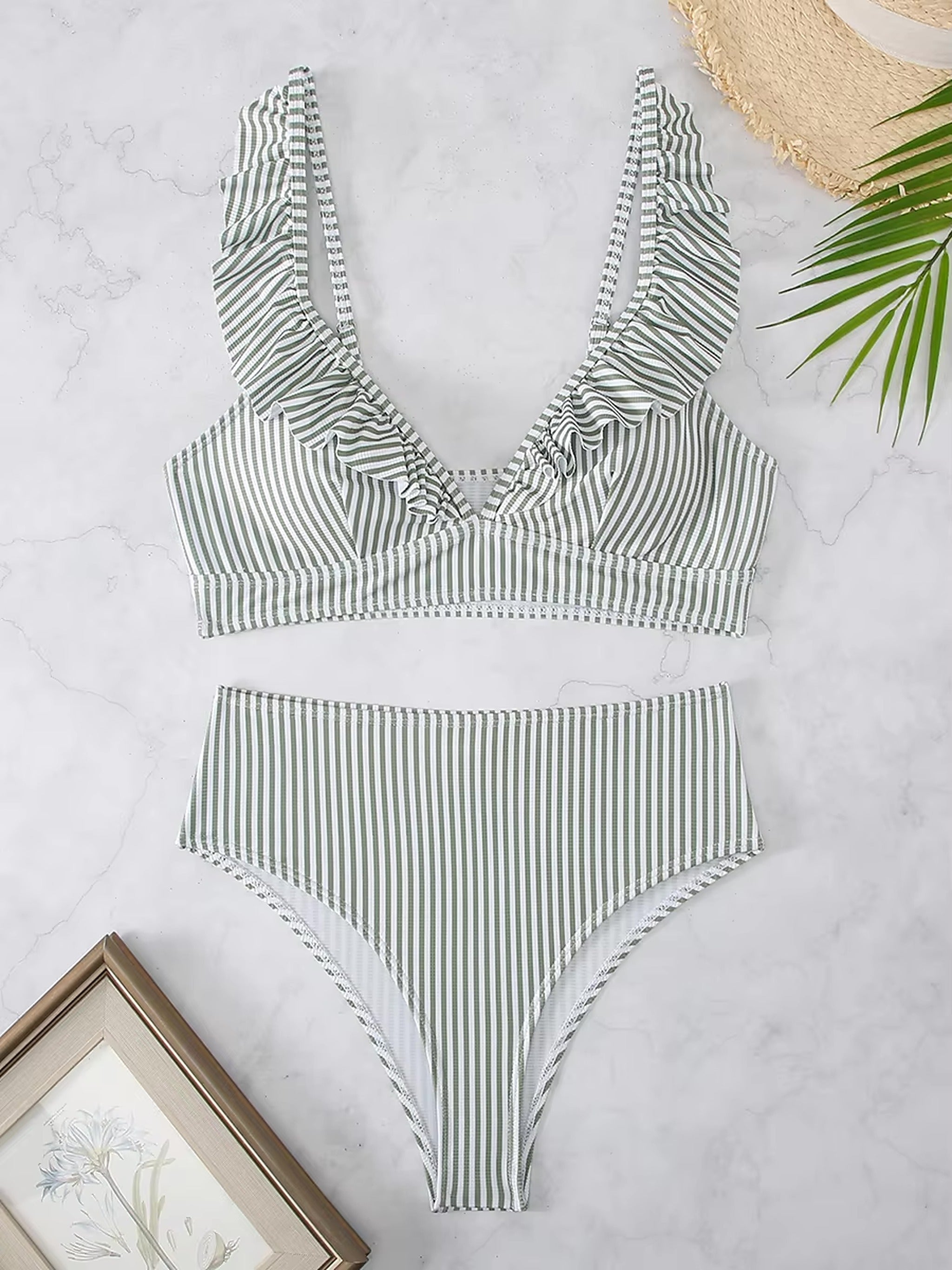 Green and white striped bikini with ruffled neckline and high-waisted bottoms on marble background with beach accessories.