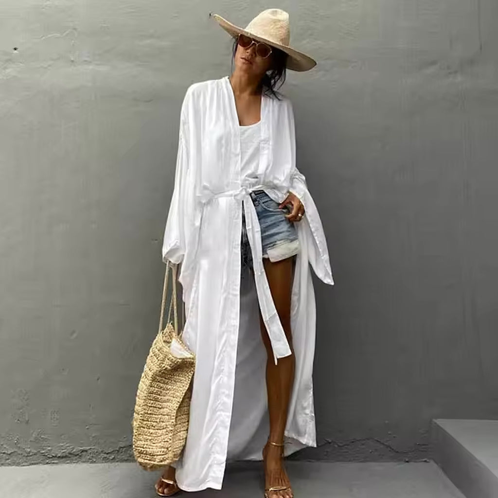 Woman wearing white linen cover-up over striped swimsuit with straw hat and beach bag