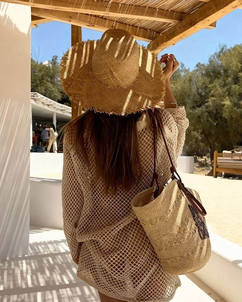 Woman wearing Saltwild knit bikini with matching cover-up at sunny terrace, holding straw hat and beach bag.