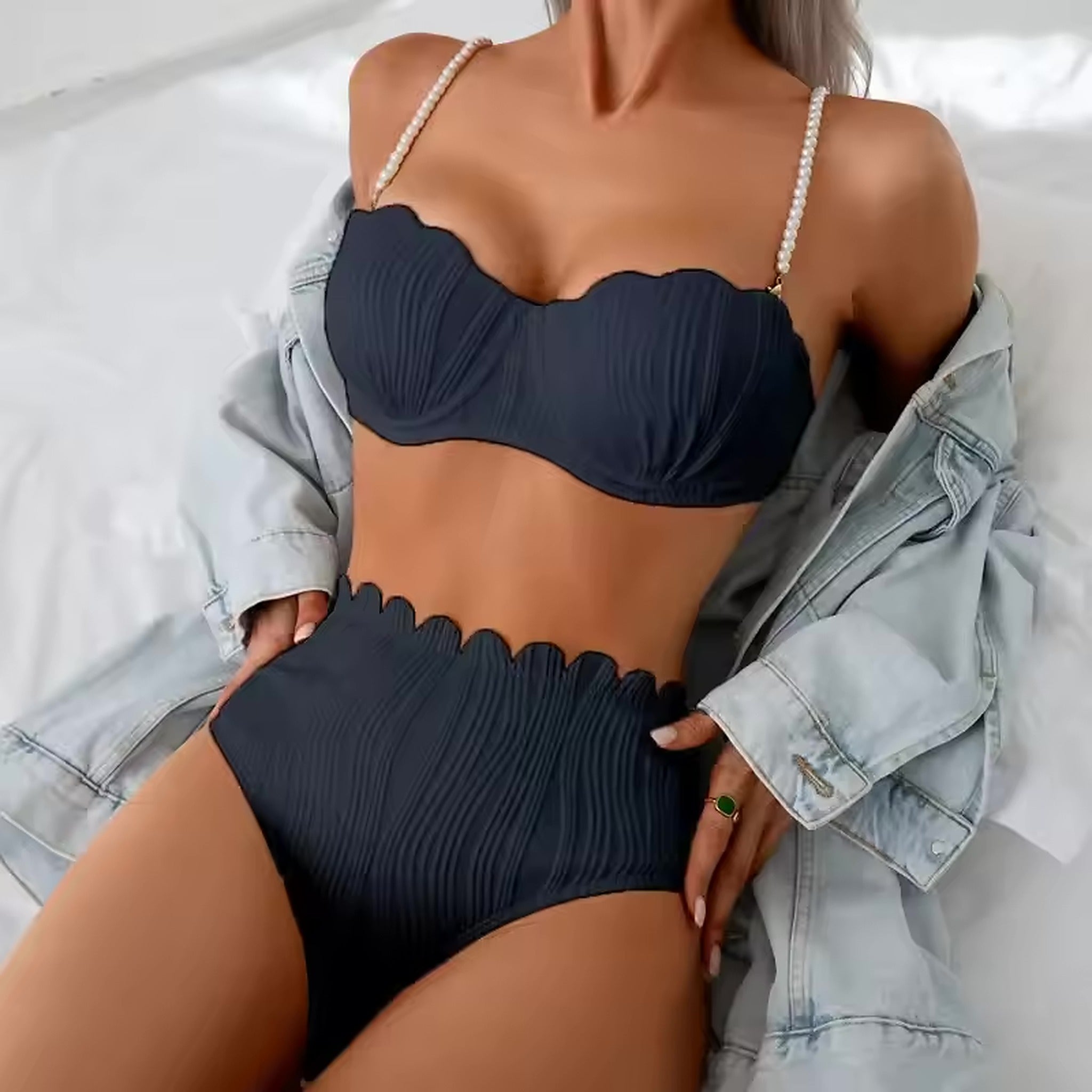 Woman wearing navy textured bikini with pearl-white straps and scalloped neckline, paired with light denim jacket.